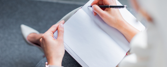 cropped shot of young woman writing in blank notepad at home