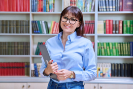 Portrait of confident female teacher mentor counselor social worker educator holding laptop inside library in educational building. Female professional education training sociology mental health