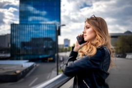 Young businesswoman talking on phone among office buildings and modern city